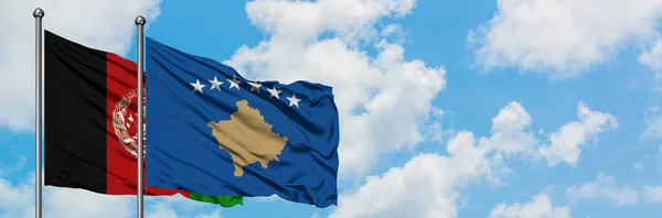 Afganistan i Kosowo flagi machając w wiatr przed białym pochmurno błękitne niebo razem. Koncepcja dyplomacji, stosunki międzynarodowe. — Zdjęcie stockowe