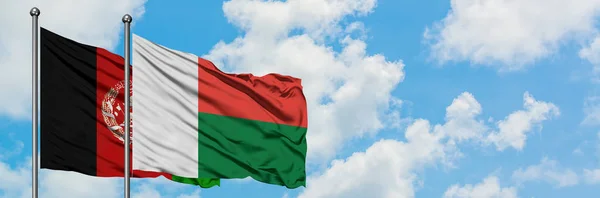 Bandera de Afganistán y Madagascar ondeando en el viento contra el cielo azul nublado blanco juntos. Concepto diplomático, relaciones internacionales . — Foto de Stock