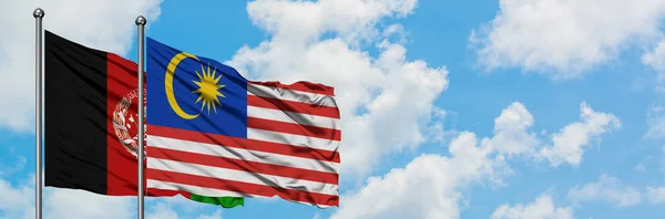 Afghanistan e Malaysia sventolano bandiera nel vento contro bianco cielo blu nuvoloso insieme. Concetto di diplomazia, relazioni internazionali . — Foto Stock