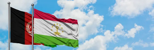 Bandera de Afganistán y Tayikistán ondeando en el viento contra el cielo azul nublado blanco juntos. Concepto diplomático, relaciones internacionales . — Foto de Stock