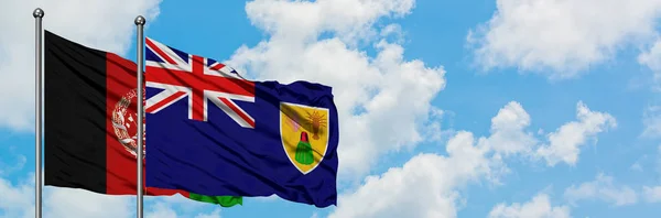 Bandera de Afganistán y las Islas Turcas y Caicos ondeando en el viento contra el cielo azul nublado blanco juntos. Concepto diplomático, relaciones internacionales . — Foto de Stock
