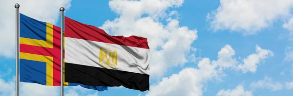 Islas Aland y la bandera de Egipto ondeando en el viento contra el cielo azul nublado blanco juntos. Concepto diplomático, relaciones internacionales . — Foto de Stock