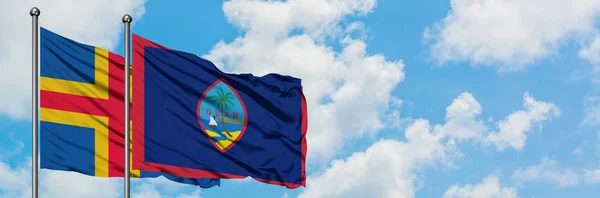 Islas Aland y la bandera de Guam ondeando en el viento contra el cielo azul nublado blanco juntos. Concepto diplomático, relaciones internacionales . — Foto de Stock