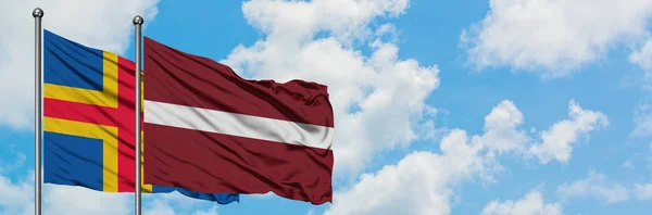 Wyspy Alandzkie i Łotwa flaga machając w wiatr przed białym zachmurzone błękitne niebo razem. Koncepcja dyplomacji, stosunki międzynarodowe. — Zdjęcie stockowe
