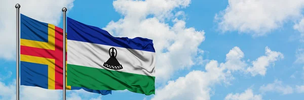 Le isole Aland e la bandiera del Lesotho sventolano insieme nel vento contro il bianco cielo blu nuvoloso. Concetto di diplomazia, relazioni internazionali . — Foto Stock