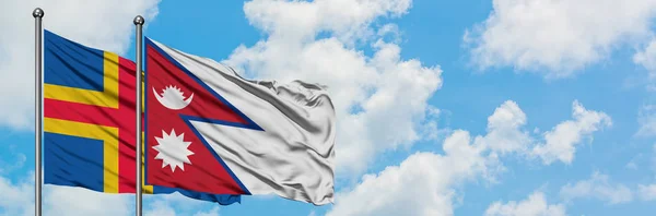 Bandera de las Islas Aland y Nepal ondeando en el viento contra el cielo azul nublado blanco juntos. Concepto diplomático, relaciones internacionales . — Foto de Stock
