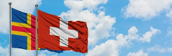 Alandské ostrovy a švýcarská vlajka mávajících větrem proti bíle zatažené modré obloze. Diplomacie, mezinárodní vztahy. — Stock fotografie