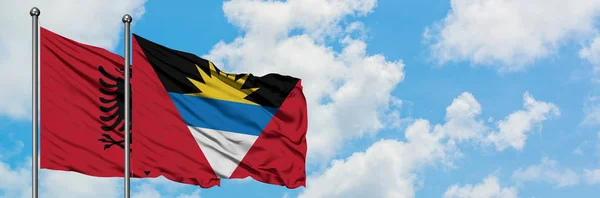 Albania y Antigua y Barbuda ondean en el viento contra el cielo azul nublado blanco juntos. Concepto diplomático, relaciones internacionales . — Foto de Stock