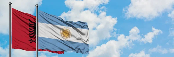 Bandera de Albania y Argentina ondeando en el viento contra el cielo azul nublado blanco juntos. Concepto diplomático, relaciones internacionales . — Foto de Stock