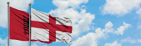 Albánie a anglická vlajka se ve větru vlnící na bíle zatažené modré obloze. Diplomacie, mezinárodní vztahy. — Stock fotografie