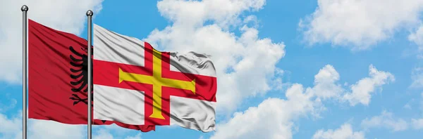 Albania e Guernsey sventolano insieme la bandiera contro il bianco cielo blu nuvoloso. Concetto di diplomazia, relazioni internazionali . — Foto Stock