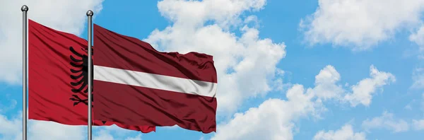 Albanien och Lettland flagga vifta i vinden mot vit grumlig blå himmel tillsammans. Diplomatisk koncept, internationella relationer. — Stockfoto