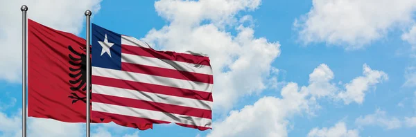 Arnavutluk ve Liberya bayrağı birlikte beyaz bulutlu mavi gökyüzüne karşı rüzgarda sallayarak. Diplomasi kavramı, uluslararası ilişkiler. — Stok fotoğraf
