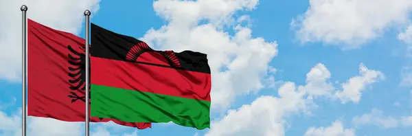 Bandera de Albania y Malawi ondeando en el viento contra el cielo azul nublado blanco juntos. Concepto diplomático, relaciones internacionales . — Foto de Stock