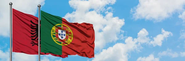 Albanien och Portugal flagga vinka i vinden mot vit grumlig blå himmel tillsammans. Diplomatisk koncept, internationella relationer. — Stockfoto