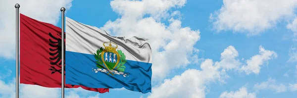 Bandera de Albania y San Marino ondeando en el viento contra el cielo azul nublado blanco juntos. Concepto diplomático, relaciones internacionales . — Foto de Stock