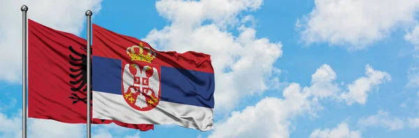 Bandera de Albania y Serbia ondeando en el viento contra el cielo azul nublado blanco juntos. Concepto diplomático, relaciones internacionales . — Foto de Stock