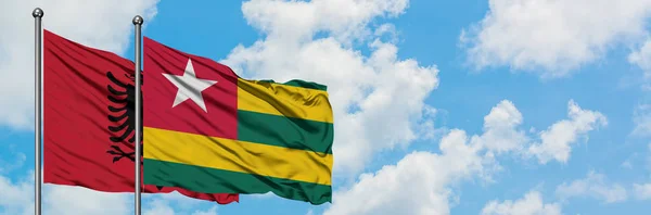 Bandera de Albania y Togo ondeando en el viento contra el cielo azul nublado blanco juntos. Concepto diplomático, relaciones internacionales . —  Fotos de Stock