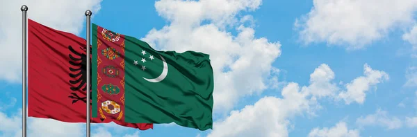 Bandera de Albania y Turkmenistán ondeando en el viento contra el cielo azul nublado blanco juntos. Concepto diplomático, relaciones internacionales . — Foto de Stock
