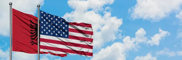 Albânia e Estados Unidos acenando com a bandeira no vento contra o céu azul nublado branco juntos. Conceito de diplomacia, relações internacionais . — Fotografia de Stock