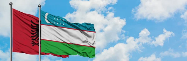 Albanien und Usbekistan schwenken gemeinsam die Flagge im Wind vor dem wolkenverhangenen blauen Himmel. Diplomatie-Konzept, internationale Beziehungen. — Stockfoto