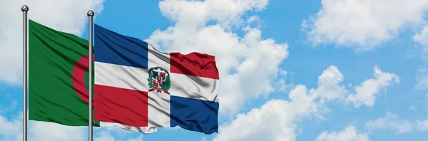 Bandera de Argelia y República Dominicana ondeando en el viento contra el cielo azul nublado blanco juntos. Concepto diplomático, relaciones internacionales . — Foto de Stock