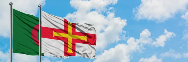 Bandera de Argelia y Guernsey ondeando en el viento contra el cielo azul nublado blanco juntos. Concepto diplomático, relaciones internacionales . — Foto de Stock