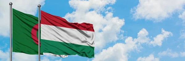Bandera de Argelia y Hungría ondeando en el viento contra el cielo azul nublado blanco juntos. Concepto diplomático, relaciones internacionales . — Foto de Stock