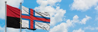 Angola ve Faroe Adaları bayrağı birlikte beyaz bulutlu mavi gökyüzüne karşı rüzgarda sallayarak. Diplomasi kavramı, uluslararası ilişkiler.