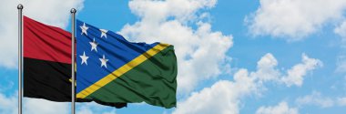 Angola ve Solomon Adaları bayrağı birlikte beyaz bulutlu mavi gökyüzüne karşı rüzgarda sallayarak. Diplomasi kavramı, uluslararası ilişkiler.