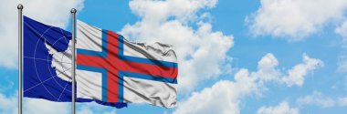 Antarktika ve Faroe Adaları bayrağı birlikte beyaz bulutlu mavi gökyüzüne karşı rüzgarda sallayarak. Diplomasi kavramı, uluslararası ilişkiler.