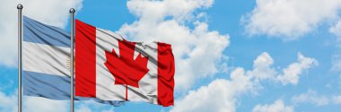 Arjantin ve Kanada bayrağı birlikte beyaz bulutlu mavi gökyüzüne karşı rüzgarda sallayarak. Diplomasi kavramı, uluslararası ilişkiler.