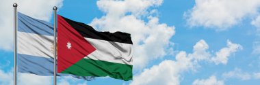 Arjantin ve Ürdün bayrağı birlikte beyaz bulutlu mavi gökyüzüne karşı rüzgarda sallayarak. Diplomasi kavramı, uluslararası ilişkiler.