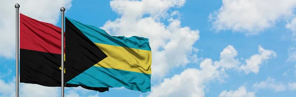 Bandera de Angola y Bahamas ondeando en el viento contra el cielo azul nublado blanco juntos. Concepto diplomático, relaciones internacionales . — Foto de Stock