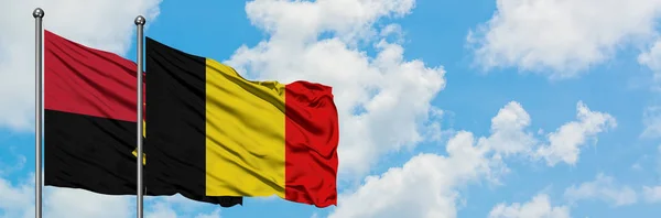 Bandera de Angola y Bélgica ondeando en el viento contra el cielo azul nublado blanco juntos. Concepto diplomático, relaciones internacionales . — Foto de Stock