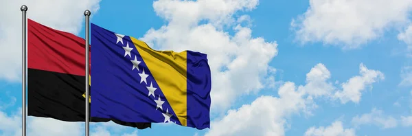 Bandera de Angola y Bosnia Herzegovina ondeando en el viento contra el cielo azul nublado blanco juntos. Concepto diplomático, relaciones internacionales . — Foto de Stock