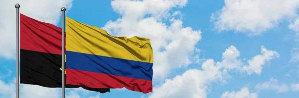 Bandera de Angola y Colombia ondeando en el viento contra el cielo azul nublado blanco juntos. Concepto diplomático, relaciones internacionales . — Foto de Stock