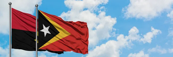 Bandera de Angola y Timor Oriental ondeando en el viento contra el cielo azul nublado blanco juntos. Concepto diplomático, relaciones internacionales . —  Fotos de Stock
