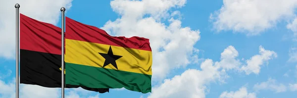 Bandera de Angola y Ghana ondeando en el viento contra el cielo azul nublado blanco juntos. Concepto diplomático, relaciones internacionales . — Foto de Stock