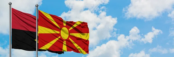 Angola și Macedonia flutură steagul în vânt împotriva cerului albastru și noros alb împreună. Conceptul de diplomație, relațiile internaționale . — Fotografie, imagine de stoc