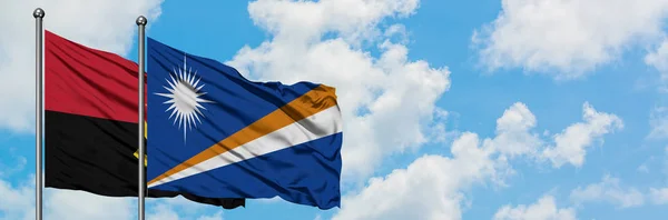 Angola and Marshall Islands flag waving in the wind against white cloudy blue sky together. Diplomacy concept, international relations.