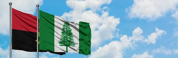 Bandera de Angola y Norfolk Island ondeando en el viento contra el cielo azul nublado blanco juntos. Concepto diplomático, relaciones internacionales . — Foto de Stock