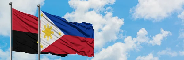 Bandeira de Angola e Filipinas agitando no vento contra o céu azul nublado branco juntos. Conceito de diplomacia, relações internacionais . — Fotografia de Stock
