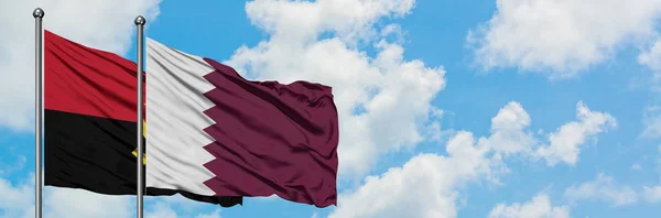 Bandera de Angola y Qatar ondeando en el viento contra el cielo azul nublado blanco juntos. Concepto diplomático, relaciones internacionales . — Foto de Stock