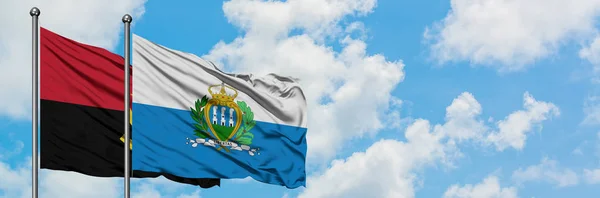 Bandera de Angola y San Marino ondeando en el viento contra el cielo azul nublado blanco juntos. Concepto diplomático, relaciones internacionales . — Foto de Stock