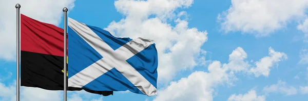 Bandeira de Angola e Escócia agitando no vento contra o céu azul nublado branco juntos. Conceito de diplomacia, relações internacionais . — Fotografia de Stock