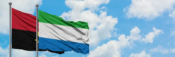 Bandera de Angola y Sierra Leona ondeando en el viento contra el cielo azul nublado blanco juntos. Concepto diplomático, relaciones internacionales . — Foto de Stock