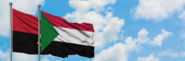 Angola und Sudan-Flagge wehen gemeinsam im Wind gegen den wolkenverhangenen blauen Himmel. Diplomatie-Konzept, internationale Beziehungen. — Stockfoto