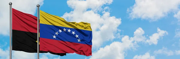 Bandera de Angola y Venezuela ondeando en el viento contra el cielo azul nublado blanco juntos. Concepto diplomático, relaciones internacionales . — Foto de Stock