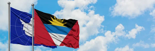 Antártida y Antigua y Barbuda ondeando en el viento contra el cielo azul nublado blanco juntos. Concepto diplomático, relaciones internacionales . — Foto de Stock